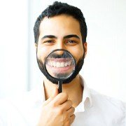 man in white dress shirt holding magnifying glass to his smile