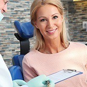 woman smiling while her dentist writes on a clipboard